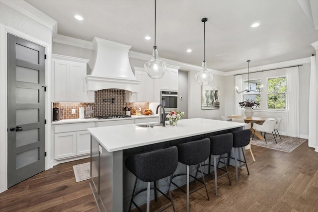 kitchen with light countertops, wall chimney range hood, a sink, and white cabinets