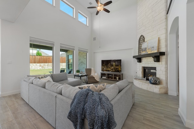 living room with a high ceiling, ceiling fan, a stone fireplace, and light hardwood / wood-style flooring