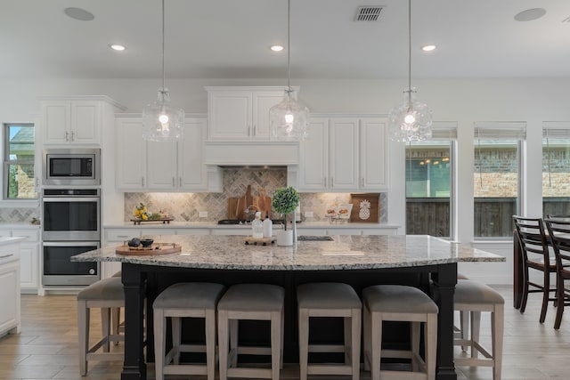 kitchen with a breakfast bar, a center island with sink, hanging light fixtures, appliances with stainless steel finishes, and white cabinetry