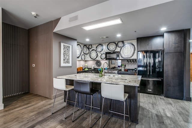 kitchen featuring a breakfast bar, a center island with sink, sink, black appliances, and hardwood / wood-style flooring