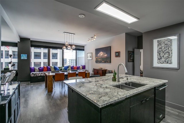 kitchen featuring light stone countertops, sink, dark hardwood / wood-style flooring, hanging light fixtures, and a center island with sink