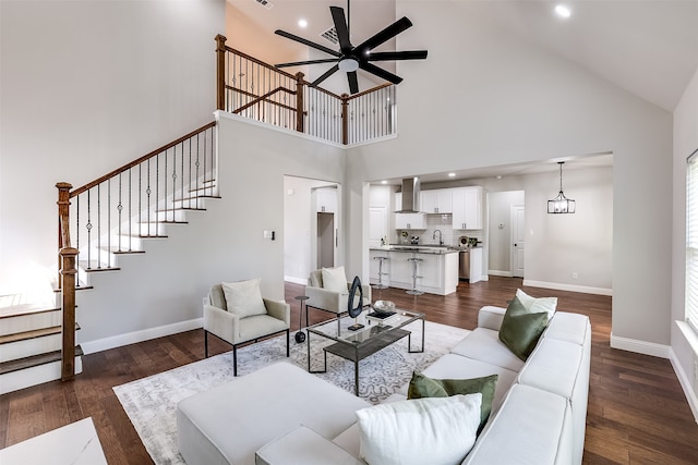 living room with sink, ceiling fan with notable chandelier, dark wood-type flooring, and high vaulted ceiling