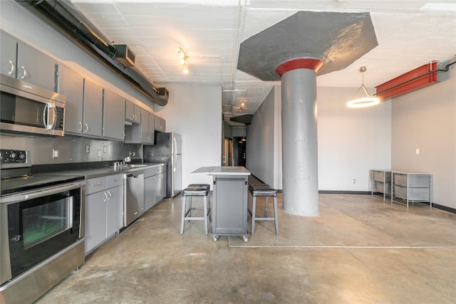 kitchen with gray cabinets, pendant lighting, appliances with stainless steel finishes, a kitchen bar, and a center island