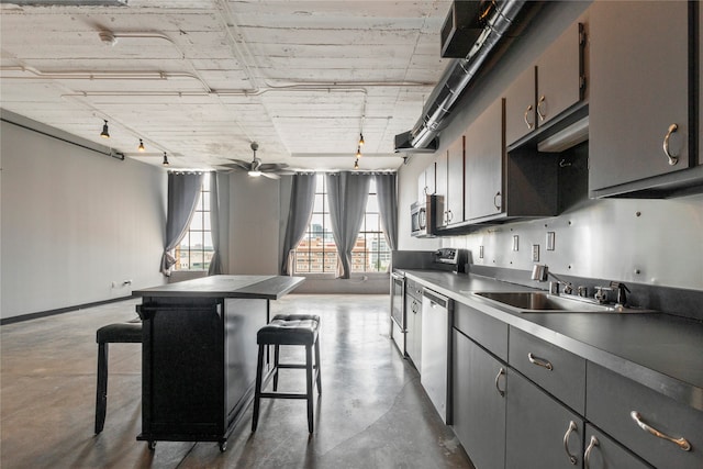 kitchen with ceiling fan, sink, a kitchen island, a kitchen breakfast bar, and stainless steel appliances