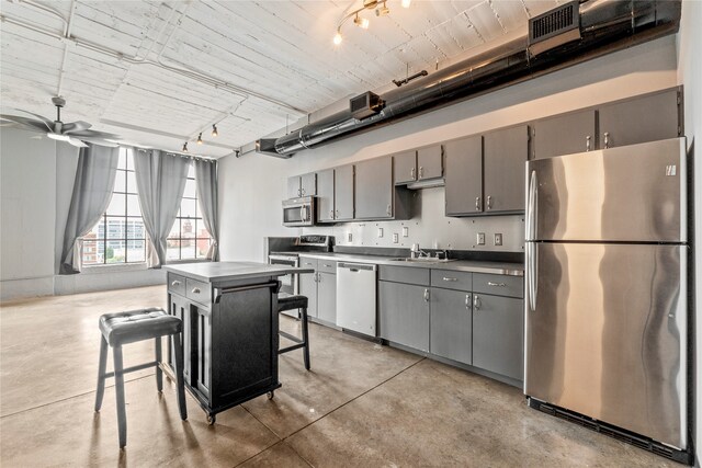 kitchen with appliances with stainless steel finishes, a kitchen island, a kitchen breakfast bar, and gray cabinetry