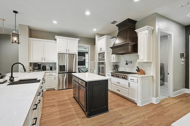 kitchen with sink, custom exhaust hood, appliances with stainless steel finishes, washer / clothes dryer, and white cabinets