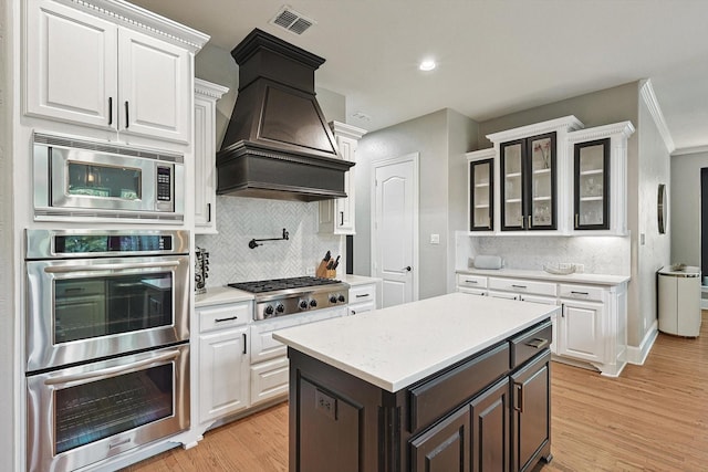 kitchen with dark brown cabinetry, appliances with stainless steel finishes, custom range hood, and white cabinets