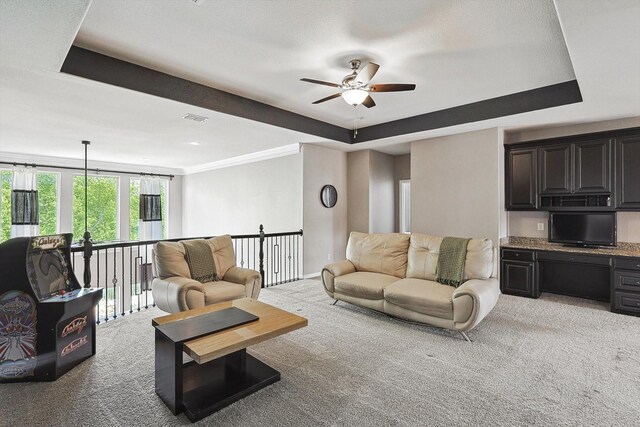 living room with crown molding, a tray ceiling, light colored carpet, and ceiling fan