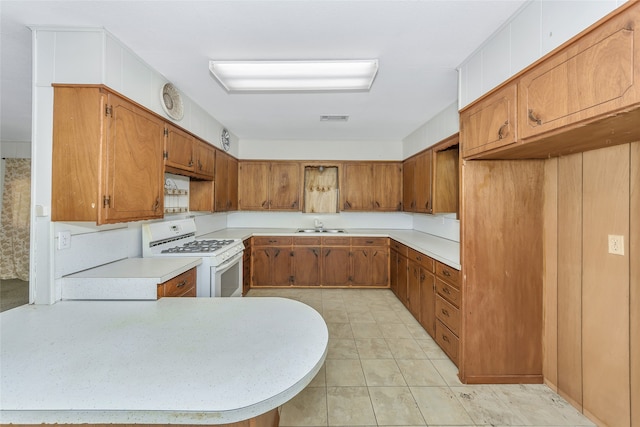 kitchen featuring kitchen peninsula, white gas range oven, sink, and light tile patterned floors