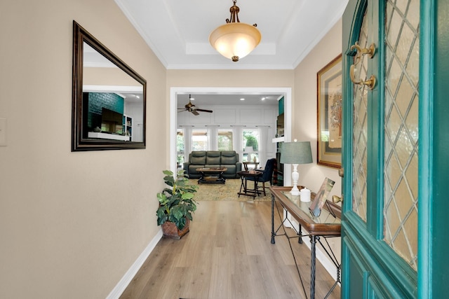 hallway featuring light wood-type flooring, crown molding, and a raised ceiling