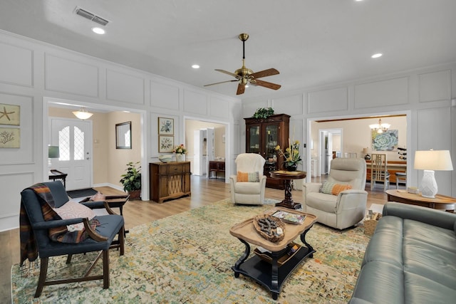 living room with ceiling fan with notable chandelier and light hardwood / wood-style floors