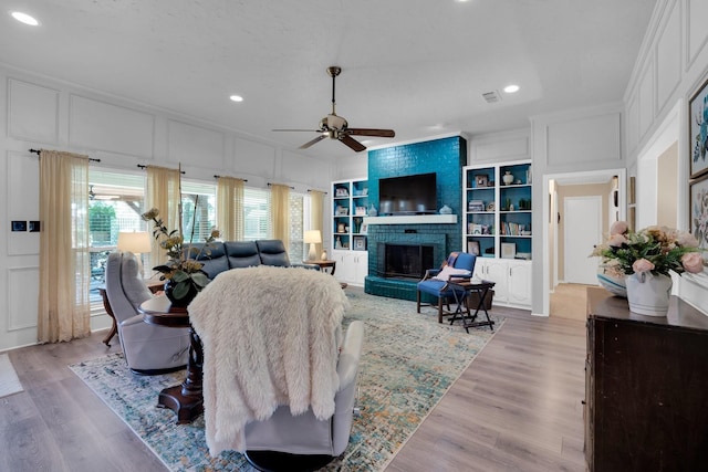 living room featuring a brick fireplace, light hardwood / wood-style floors, built in features, and ceiling fan