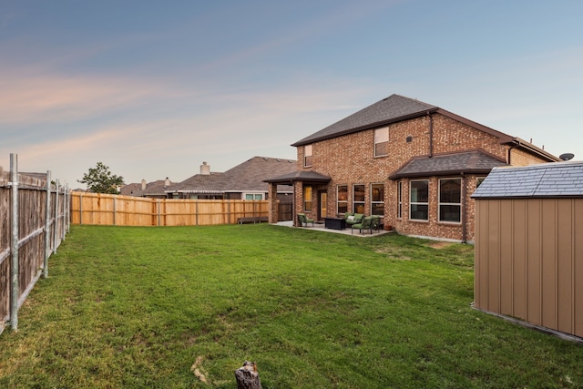 back house at dusk featuring a lawn, a patio area, and a storage shed