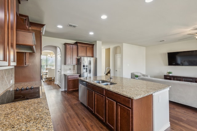 kitchen featuring stainless steel appliances, sink, light stone counters, decorative backsplash, and a kitchen island with sink