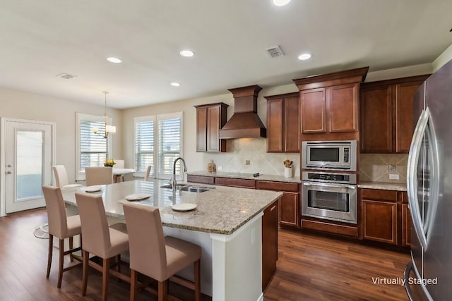 kitchen with sink, decorative light fixtures, decorative backsplash, premium range hood, and appliances with stainless steel finishes