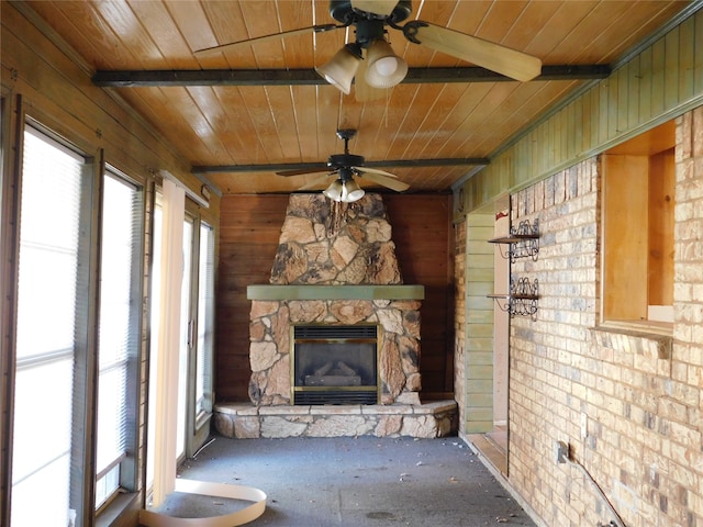 unfurnished living room featuring beam ceiling, ceiling fan, brick wall, an outdoor stone fireplace, and wood ceiling