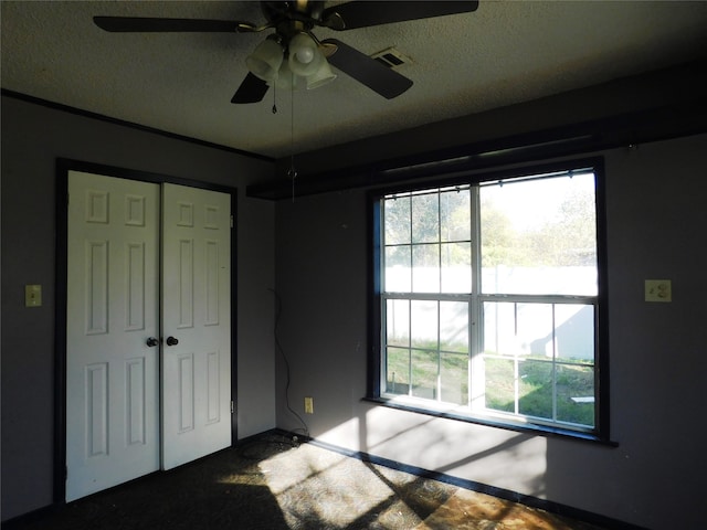 unfurnished bedroom with ceiling fan, a closet, a textured ceiling, and multiple windows