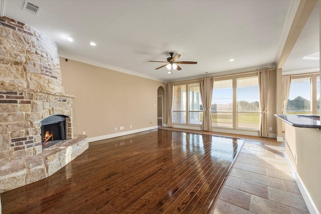 unfurnished living room featuring ornamental molding, a stone fireplace, light wood-type flooring, and ceiling fan