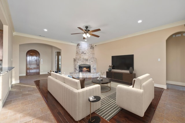 living room with ceiling fan, ornamental molding, and a stone fireplace