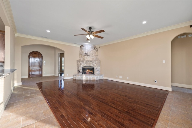 unfurnished living room with crown molding, ceiling fan, a stone fireplace, and light hardwood / wood-style flooring