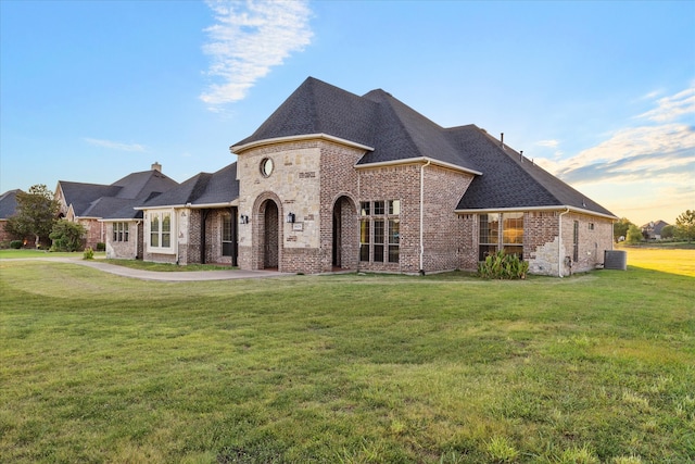 french country home featuring central AC unit and a lawn