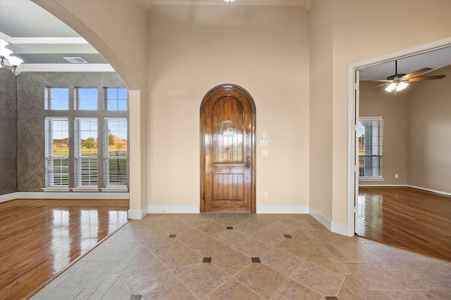 foyer entrance with a towering ceiling, ornamental molding, and light wood-type flooring