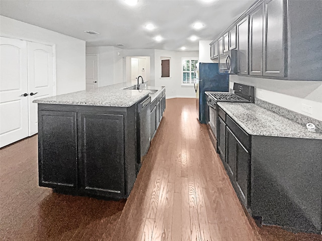 kitchen with light stone countertops, gas stove, a center island with sink, and dark hardwood / wood-style flooring