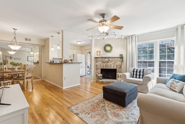 living room featuring ceiling fan, a stone fireplace, and light hardwood / wood-style flooring