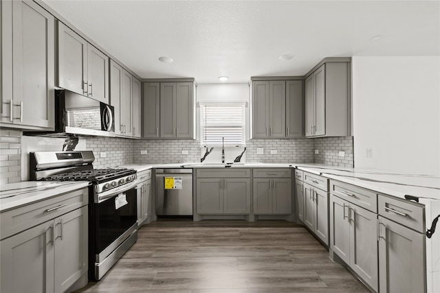 kitchen with appliances with stainless steel finishes, gray cabinets, dark wood-type flooring, and sink