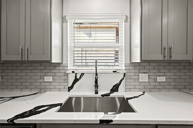 kitchen featuring gray cabinets, light stone countertops, sink, and decorative backsplash