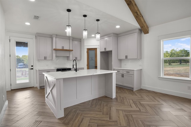 kitchen featuring tasteful backsplash, an island with sink, beam ceiling, and light stone counters