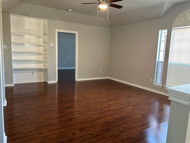 unfurnished living room with built in shelves, ceiling fan, and dark wood-type flooring