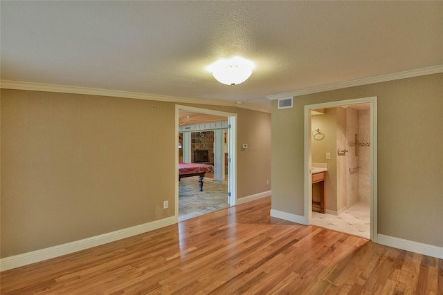 unfurnished bedroom featuring crown molding, a textured ceiling, connected bathroom, light hardwood / wood-style floors, and a tiled fireplace