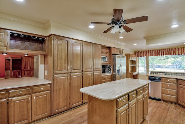 kitchen featuring light wood-type flooring, ornamental molding, stainless steel appliances, ceiling fan, and a kitchen island