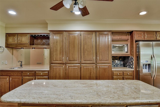 kitchen with sink, stainless steel refrigerator with ice dispenser, ceiling fan, ornamental molding, and light stone counters