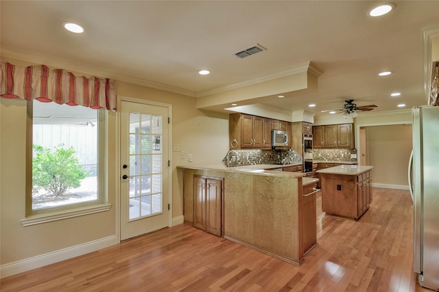 kitchen with crown molding, appliances with stainless steel finishes, tasteful backsplash, light hardwood / wood-style floors, and kitchen peninsula