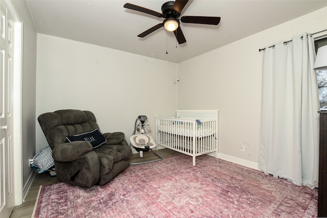 bedroom featuring a nursery area, hardwood / wood-style flooring, and ceiling fan