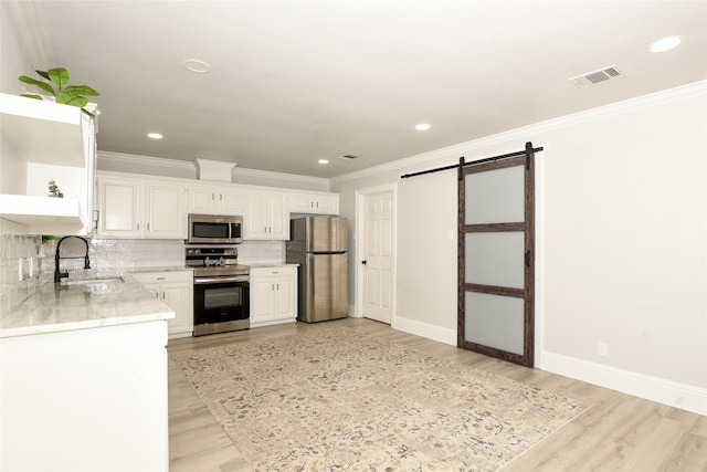 kitchen featuring stainless steel appliances, sink, white cabinetry, a barn door, and light hardwood / wood-style flooring