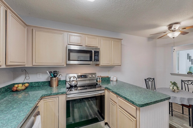 kitchen with ceiling fan, stainless steel appliances, light hardwood / wood-style floors, kitchen peninsula, and a textured ceiling