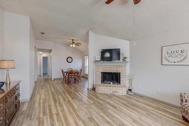 living room with ceiling fan, lofted ceiling, a brick fireplace, a textured ceiling, and light hardwood / wood-style flooring