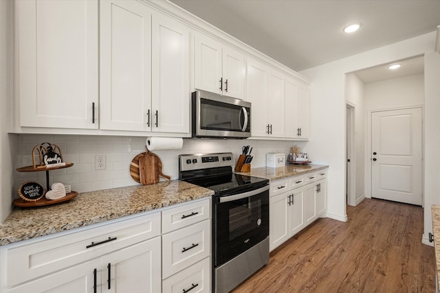 kitchen featuring backsplash, white cabinets, light hardwood / wood-style flooring, light stone counters, and stainless steel appliances