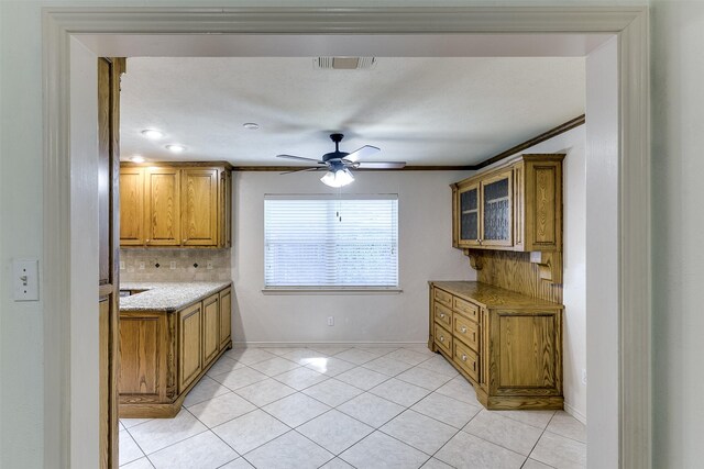 kitchen featuring light tile patterned flooring, decorative backsplash, light stone counters, ceiling fan, and crown molding