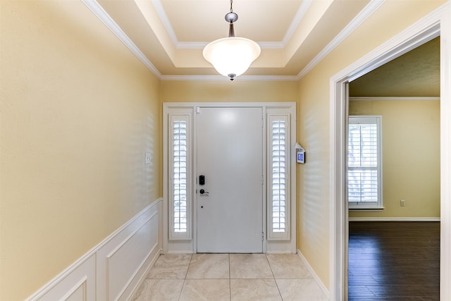 foyer entrance featuring crown molding, a decorative wall, a tray ceiling, and wainscoting