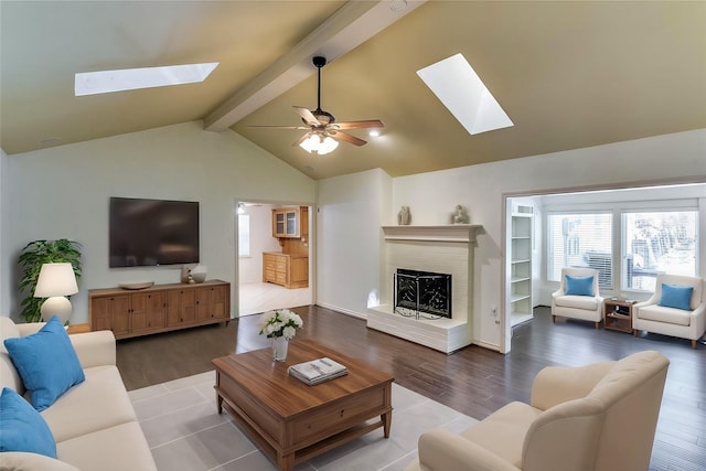 living room with vaulted ceiling with skylight, a brick fireplace, a ceiling fan, and wood finished floors