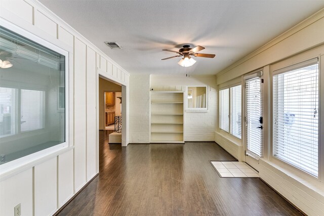 spare room featuring built in features, ceiling fan, crown molding, dark wood-type flooring, and a textured ceiling