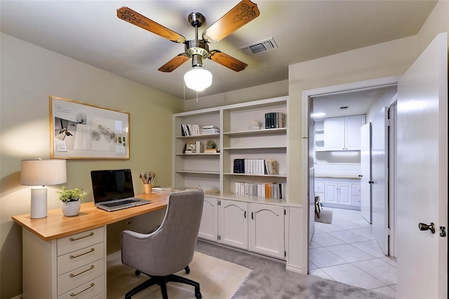 office area with visible vents, light colored carpet, built in desk, light tile patterned flooring, and a ceiling fan