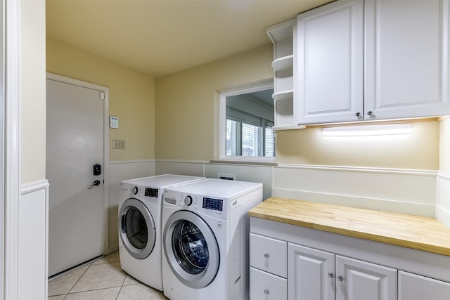 laundry area featuring washer and dryer, light tile patterned floors, cabinet space, and a wainscoted wall