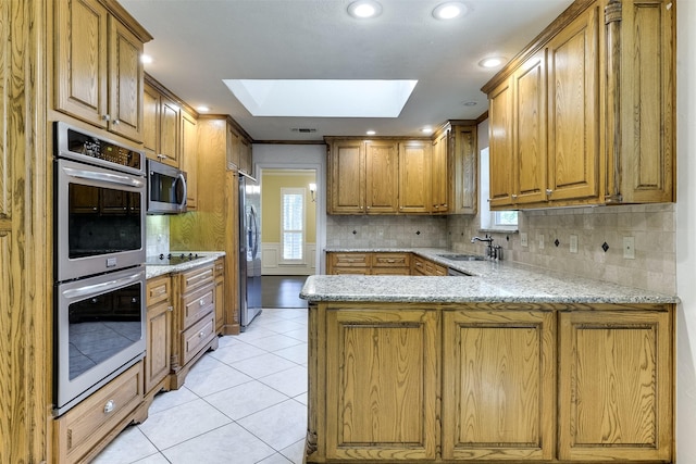 kitchen with appliances with stainless steel finishes, a skylight, a peninsula, light tile patterned flooring, and a sink