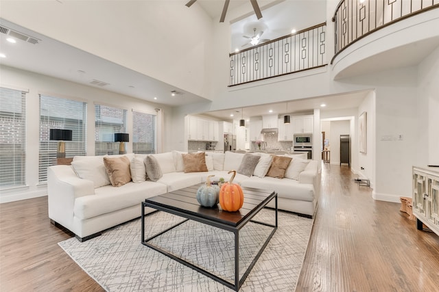 living room featuring a towering ceiling, light wood-type flooring, and ceiling fan