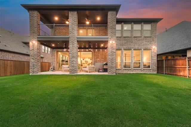 back house at dusk with an outdoor hangout area, a patio, a balcony, and a lawn